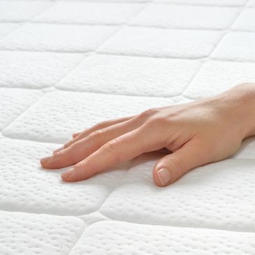A hand gently resting on a clean, textured white mattress.