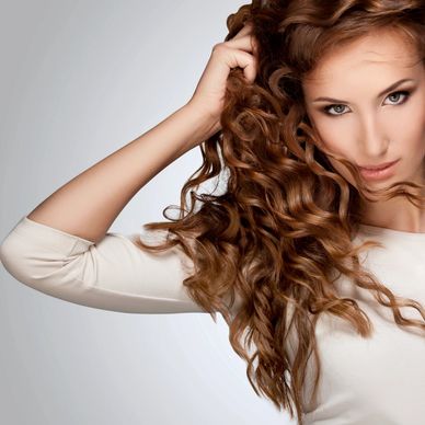 Woman with long, curly brown hair posing confidently.