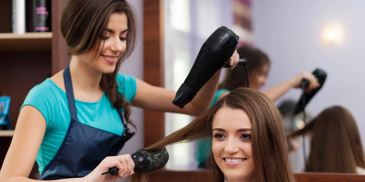 Hairdresser blow-drying a smiling woman's hair in a salon.