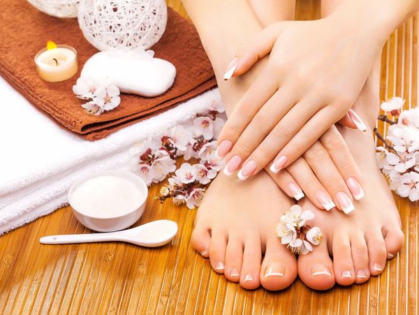 Well-manicured hands and feet with spa essentials and flowers on a wooden surface.