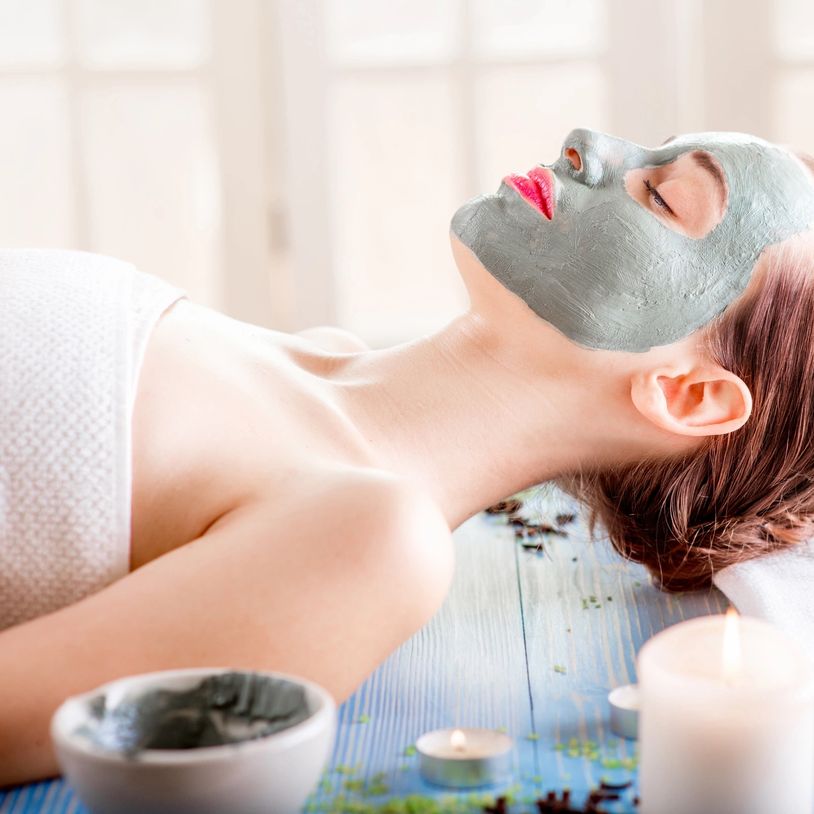 Relaxed woman with a gray facial mask lying on a spa table.