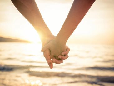 Two people holding hands at the beach.