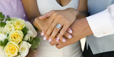 A couples hands touching showing their wedding rings surrounded by a bouquet of flowers.