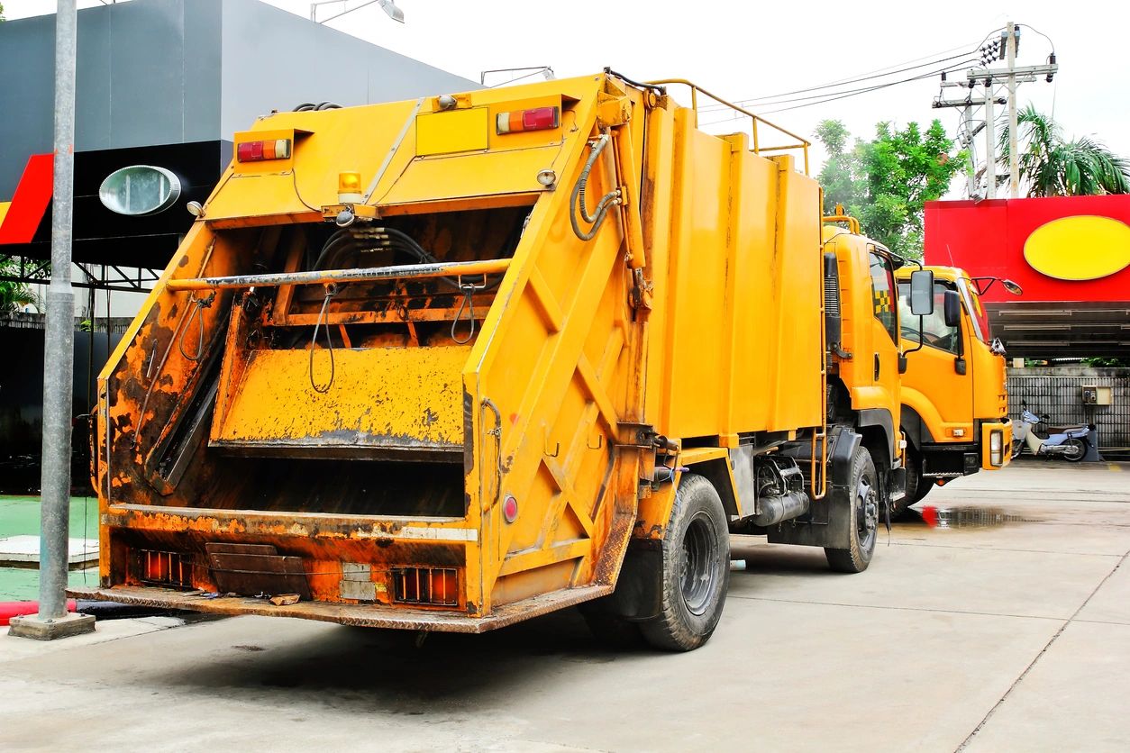 A yellow garbage truck parked outdoors near a building.