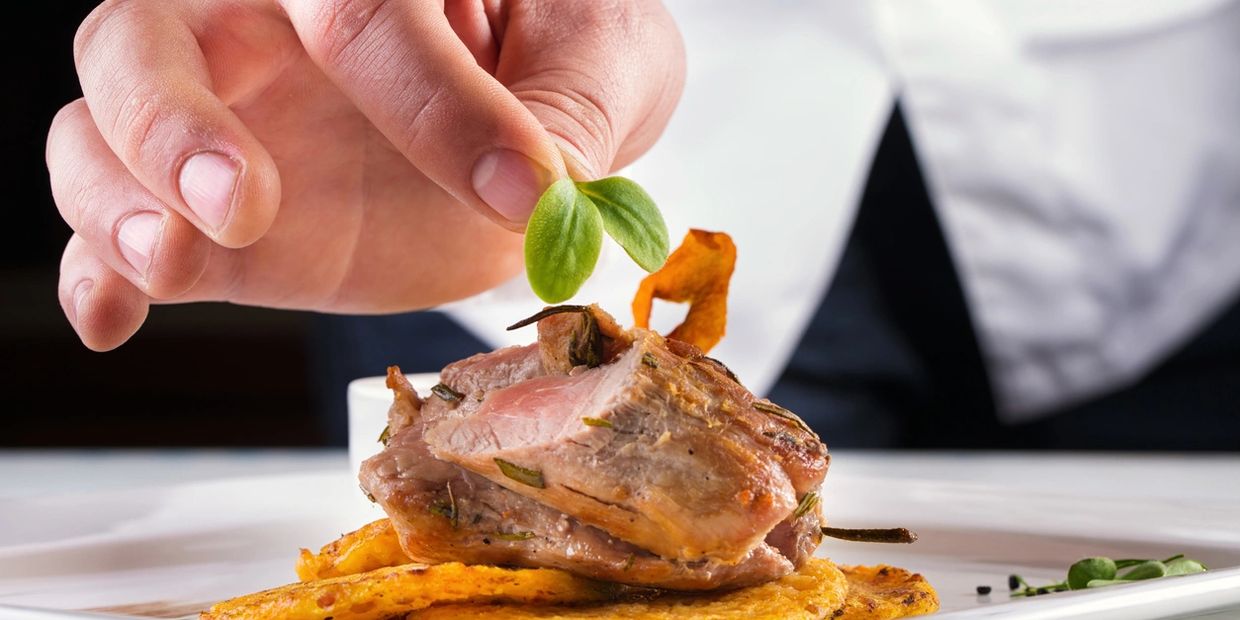 Hand garnishing cooked meat with greens on a plate.