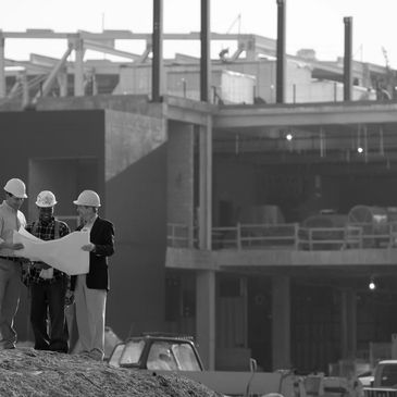 Engineers reviewing plans at a construction site with a building in progress.