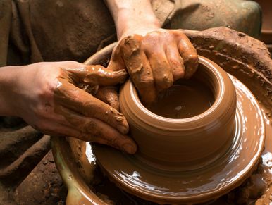 Hands shaping a clay pot on a pottery wheel.