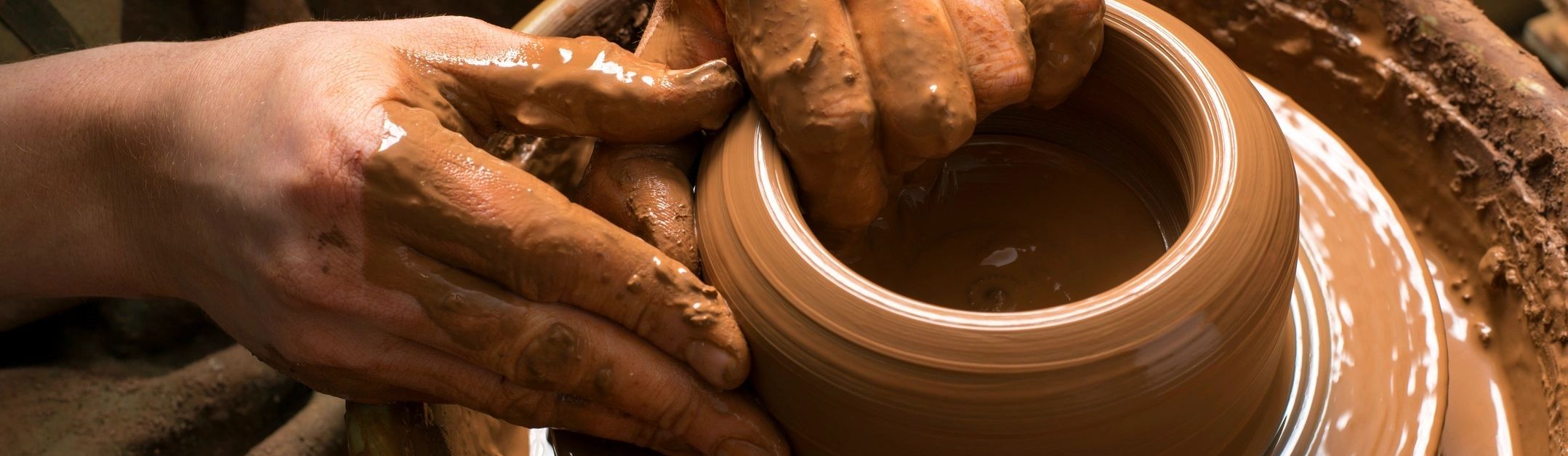 Hands shaping a clay pot on a spinning pottery wheel.