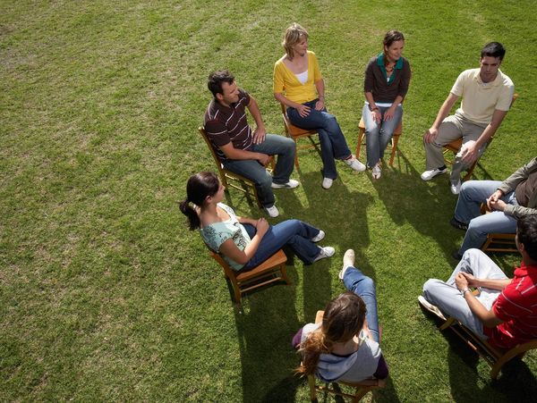 Group of people sitting in a circle on chairs outdoors.