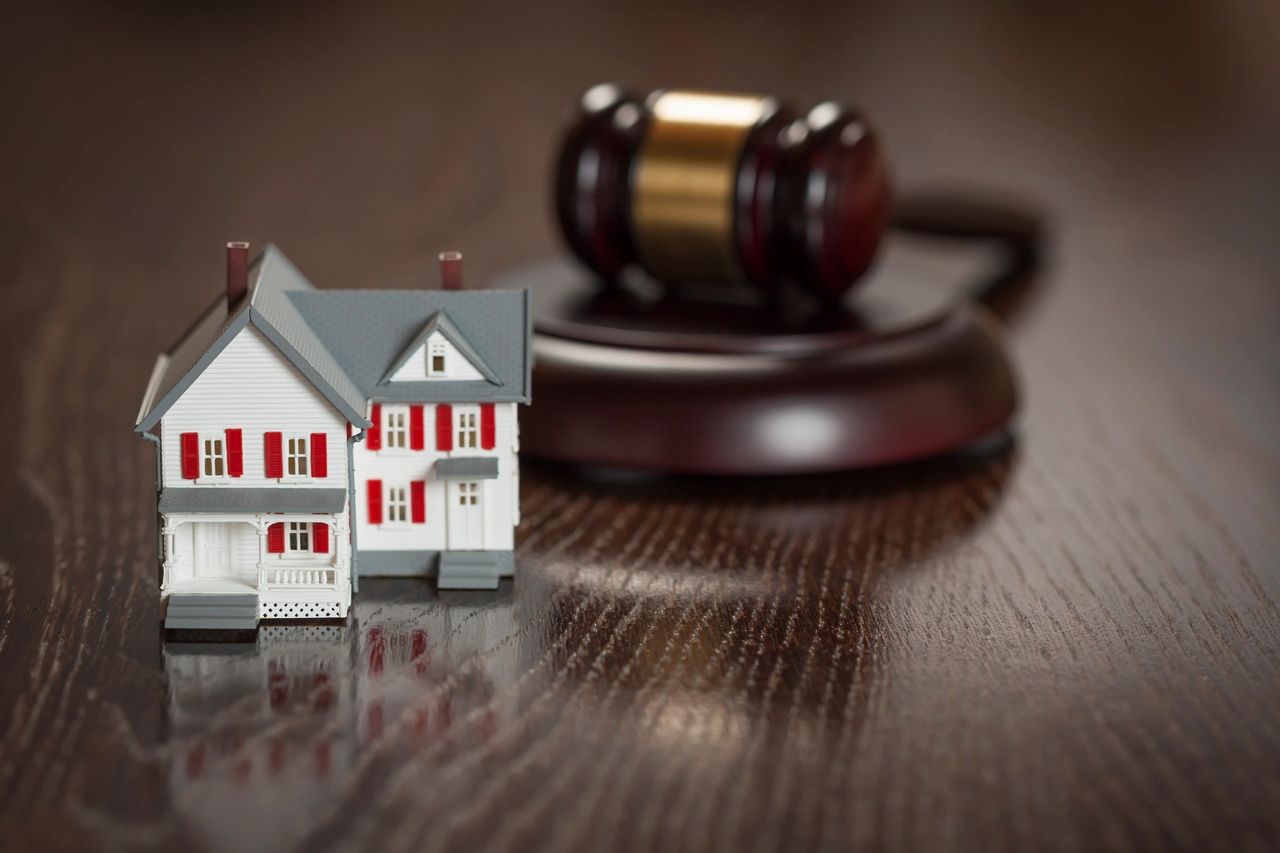 A gavel and a house figurine sit on the dark wood table top.