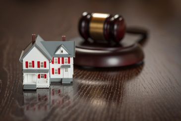 A miniature house model next to a judge's gavel on a wooden table.