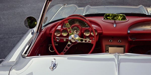 Classic car interior with red dashboard and steering wheel.
