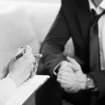 Person taking notes during a professional meeting with a suited individual.