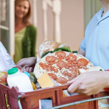 Person carrying groceries, including a heart-shaped pepperoni pizza, while another person waits.