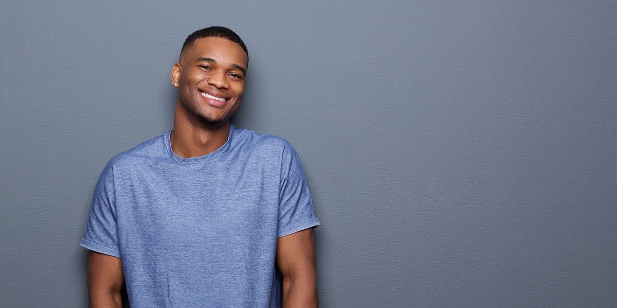 Smiling young man in a blue t-shirt against a gray wall.