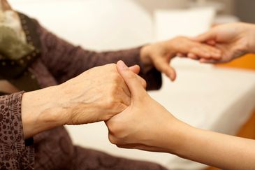 An elderly person holding hands with a younger individual, symbolizing care and support.