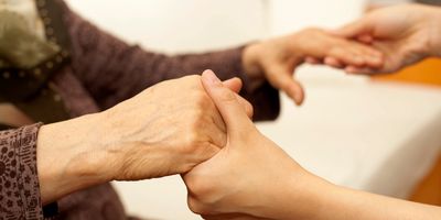 A younger person holding hands with an elderly person in a nursing home,