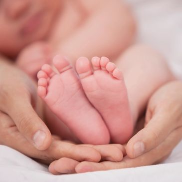Adult hands gently holding a newborn baby's feet.