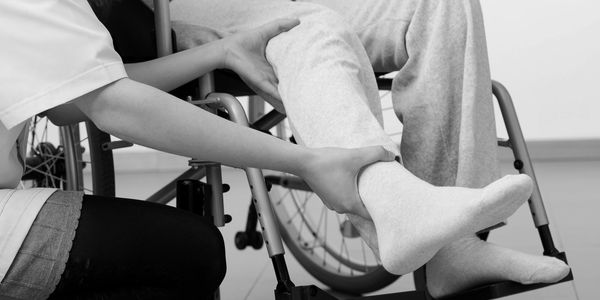 Caregiver assisting person in wheelchair with leg movement.