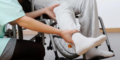 Woman assesses a man's leg who's sitting in a wheelchair. 