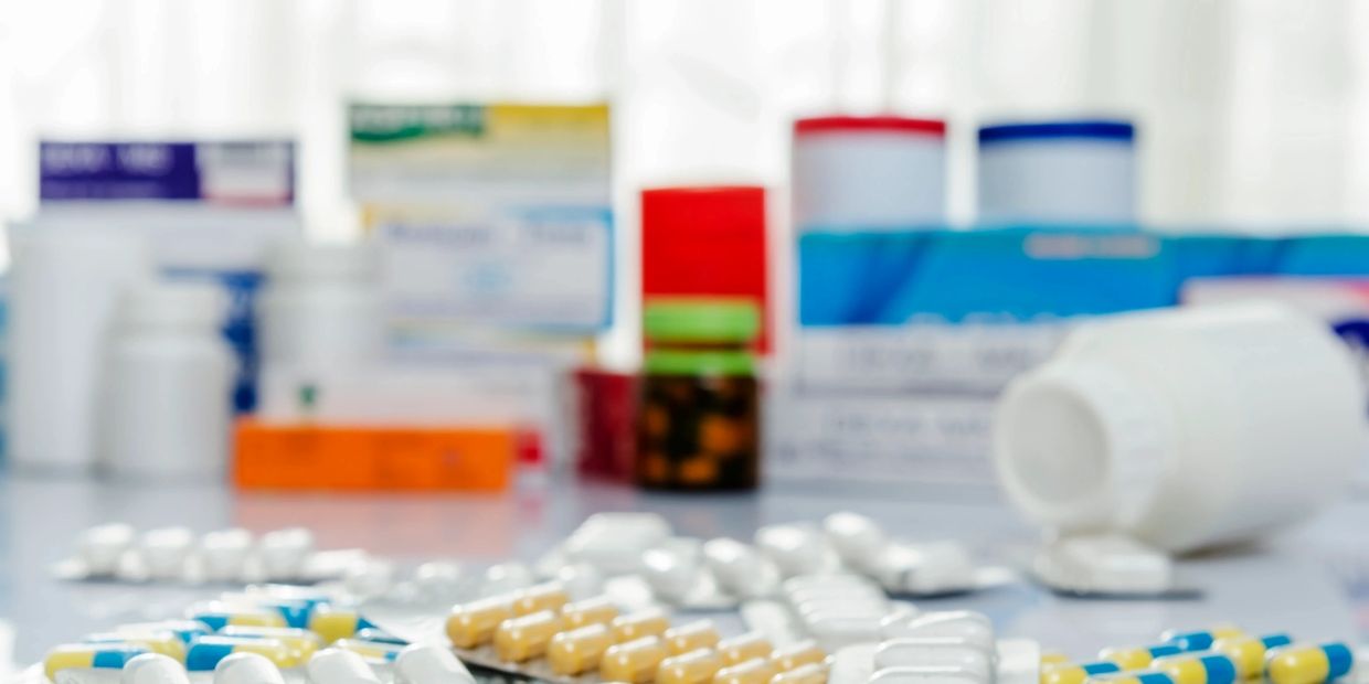 Various pills and capsules scattered with blurred medicine boxes in the background.