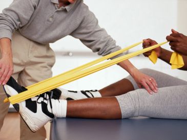 Physical therapist assisting patient with resistance band leg exercises.
