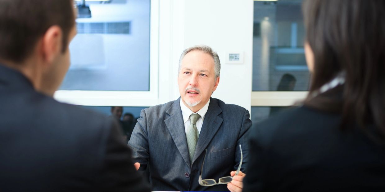 Mature man in a suit talking to two people in a meeting.