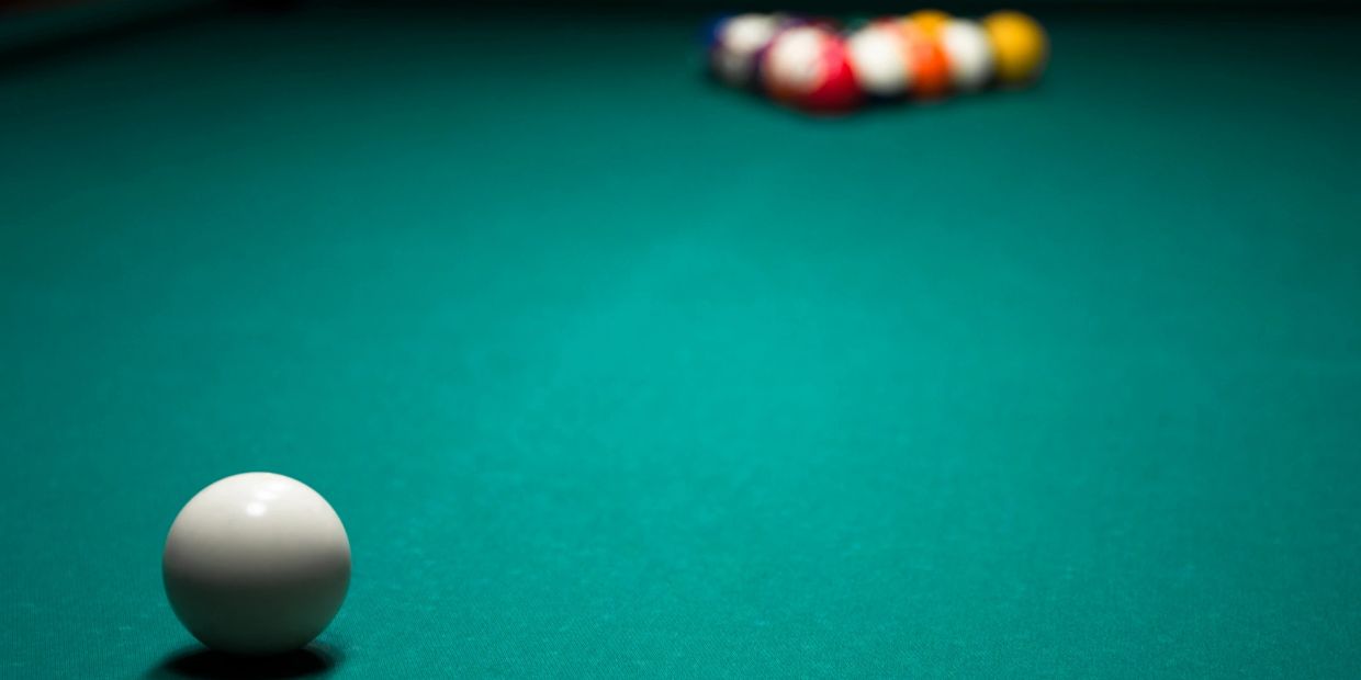 A close-up of a white cue ball on a green pool table with racked balls in the background.