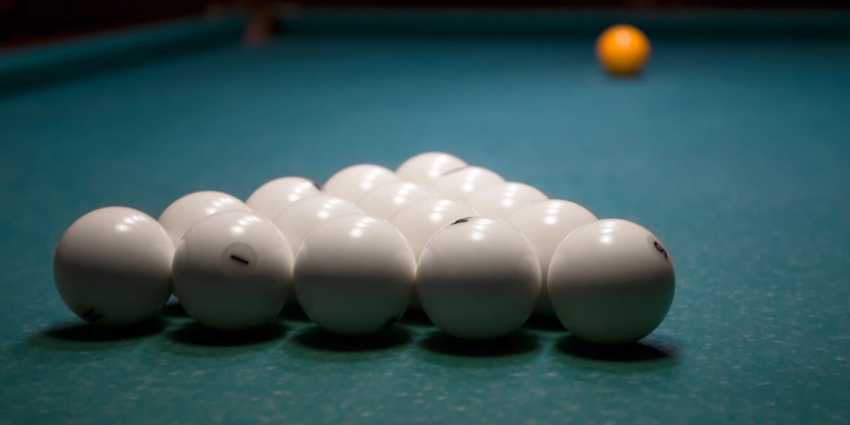 White billiard balls arranged in a triangle with an orange ball in the distance.