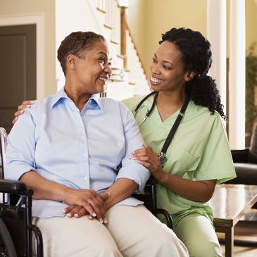 Nurse smiling and comforting an elderly woman in a wheelchair.