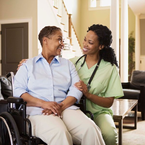 Nurse comforting elderly woman in wheelchair with warm smiles indoors.