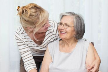 A younger woman smiling at an elderly woman with glasses.