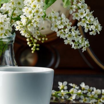 White cup with saucer and flowers in a glass vase.