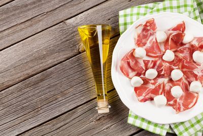 Plate of prosciutto and mozzarella with olive oil bottle on wooden table.