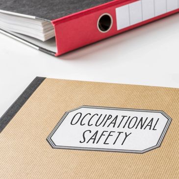 Binder and papers on a desk beside a book for Occupational Safety.
