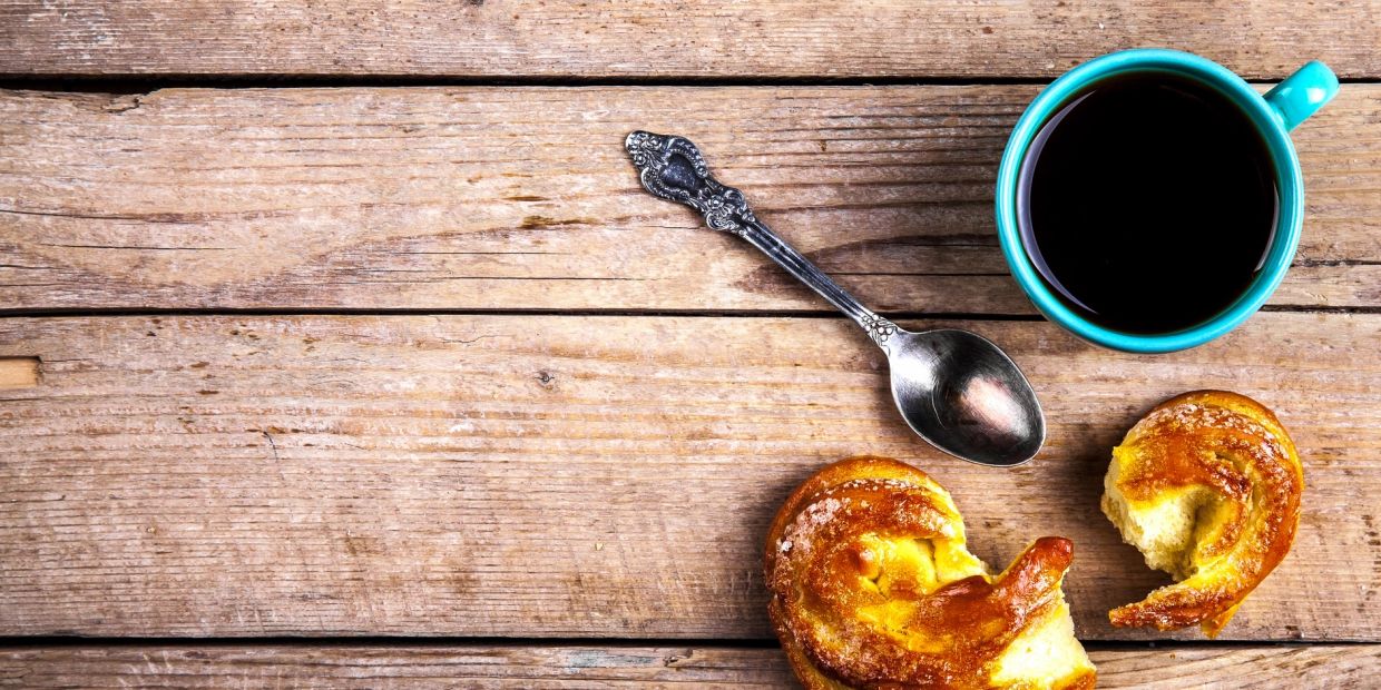 Coffee cup with a spoon and a bitten pastry on a wooden table.