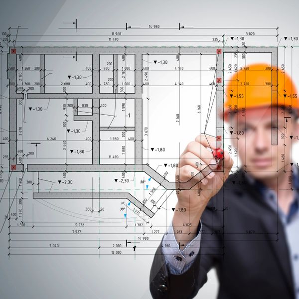 Engineer in hard hat drawing architectural blueprint with marker.