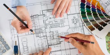 Two people working on architectural blueprints with color swatches nearby.