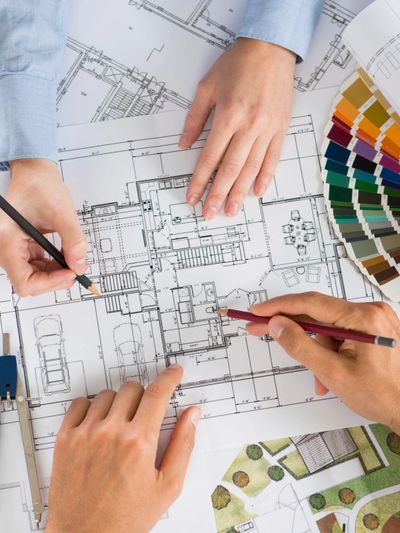 Two people working on architectural blueprints with color swatches nearby.