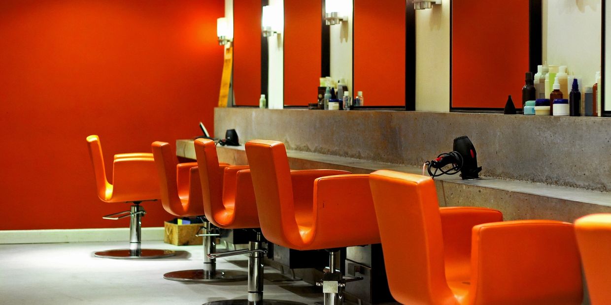 Orange salon chairs aligned in a modern hair salon with red walls.