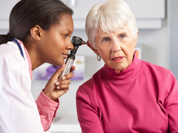 Hearing provider examines woman with an otoscope.