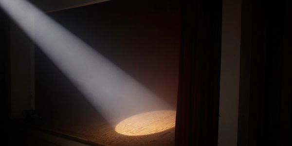 A spotlight shines on a dark empty stage with curtains.