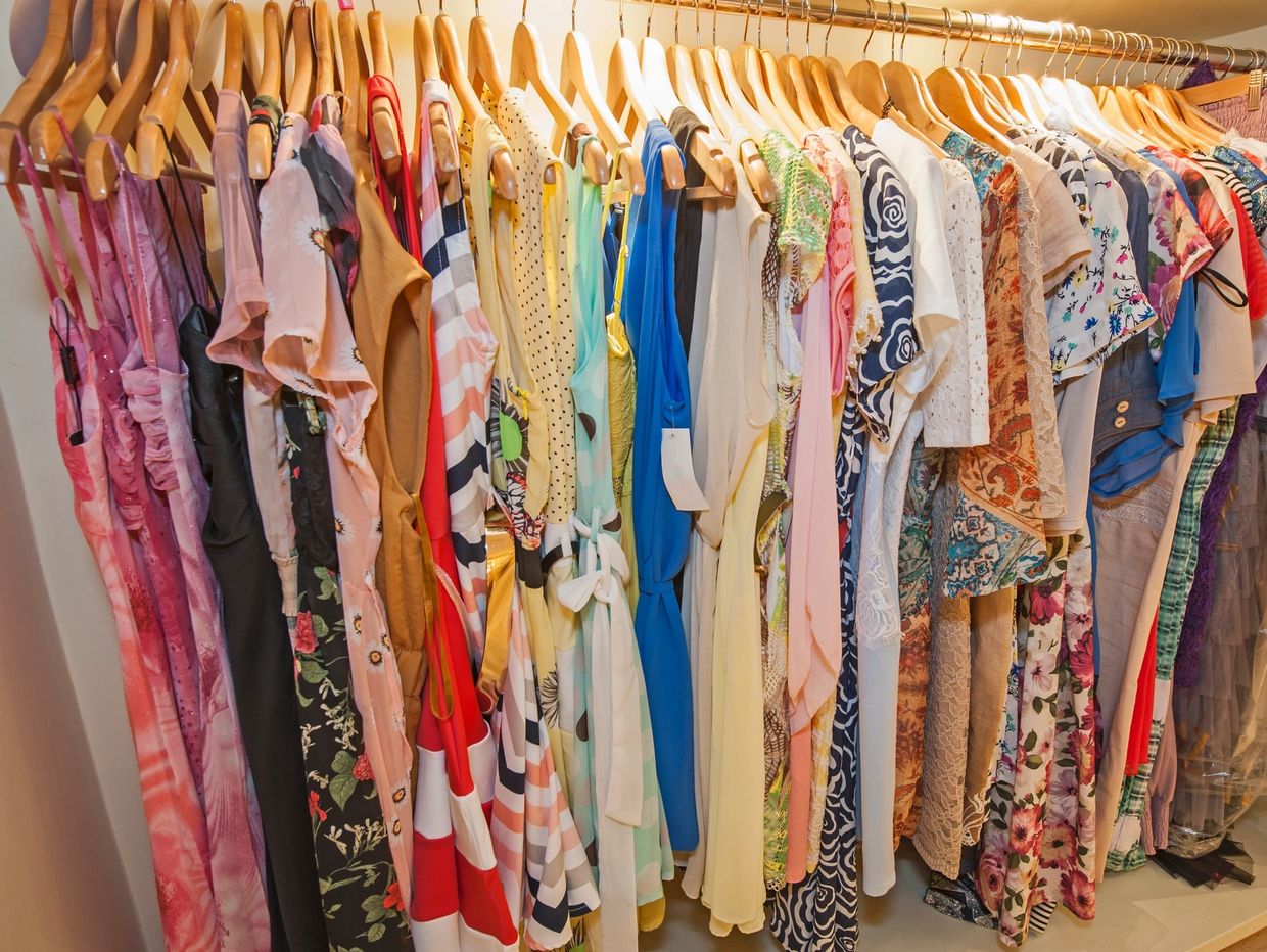 Colorful women's dresses hanging on wooden hangers in a closet.