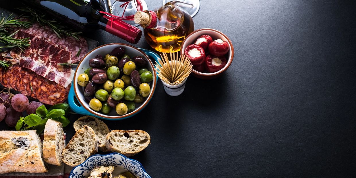 Charcuterie board with olives, bread, wine, and stuffed peppers.