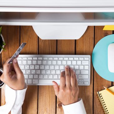 A person in front of a computer typing with right hand and holding credit card on left hand