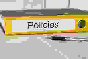 A yellow ringbinder lying on its side in front of a black and silver pen and documents.