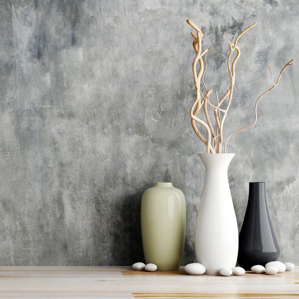 Group of three ceramic vases in various shapes and height in front of abstract grey tone wall paper.