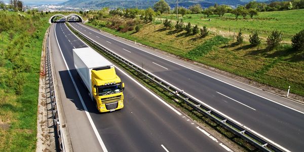 Yellow trucking attached to a trailer driving down the highway.