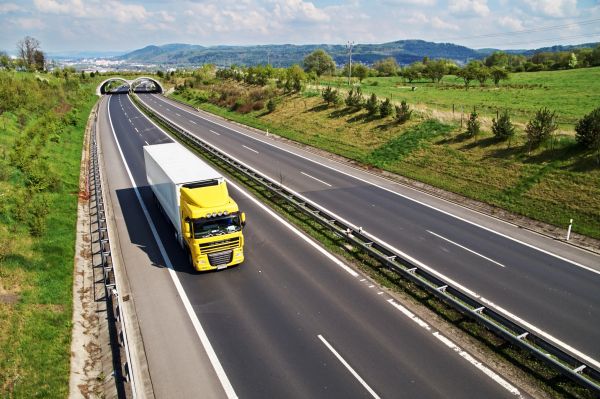 Yellow truck driving on a highway approaching a tunnel in a green rural area.