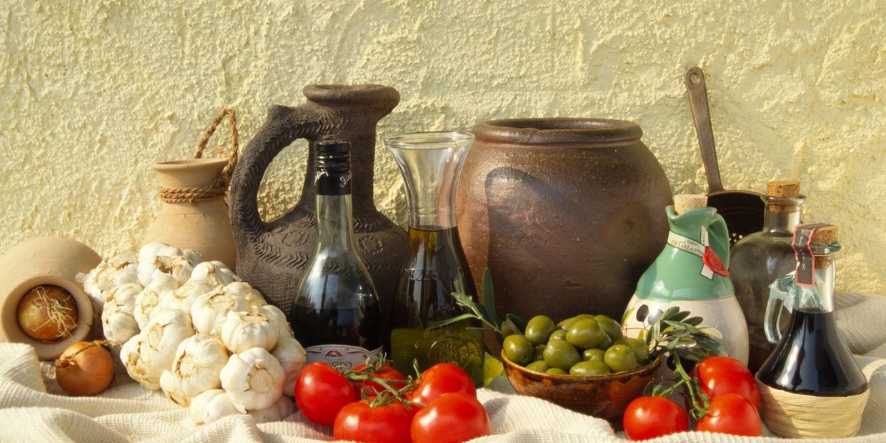 Rustic Mediterranean still life with garlic, tomatoes, olives, and clay pots.